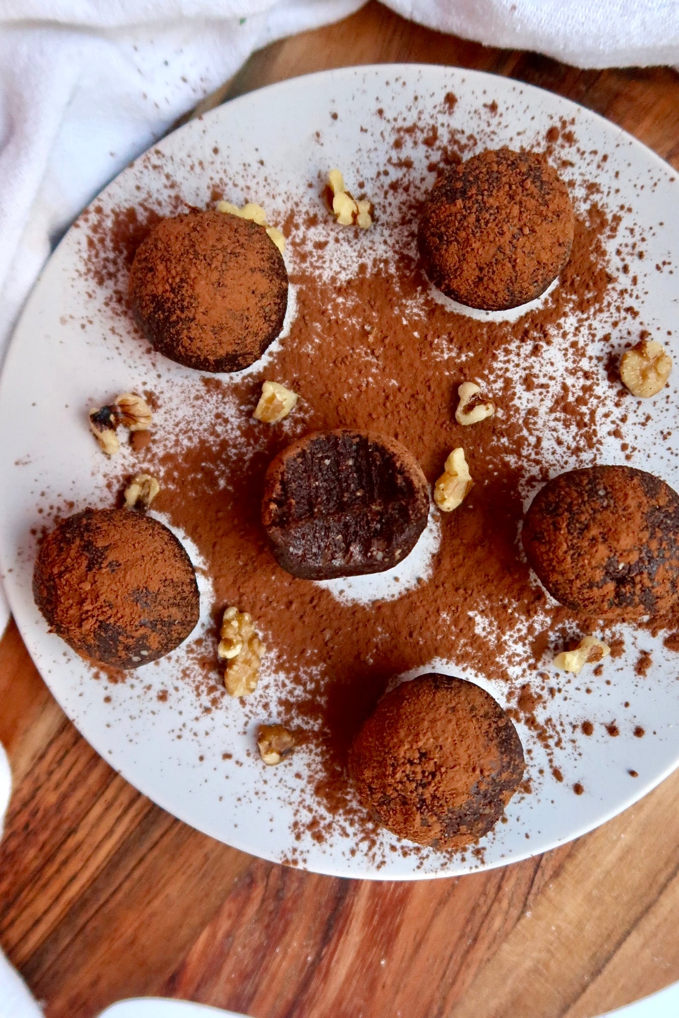 A plate of brownie energy balls with one half bitten and cocoa powder sprinkled on top.