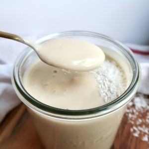 Glass jar with coconut pudding in it with coconut flakes on top and spoon scooping some.
