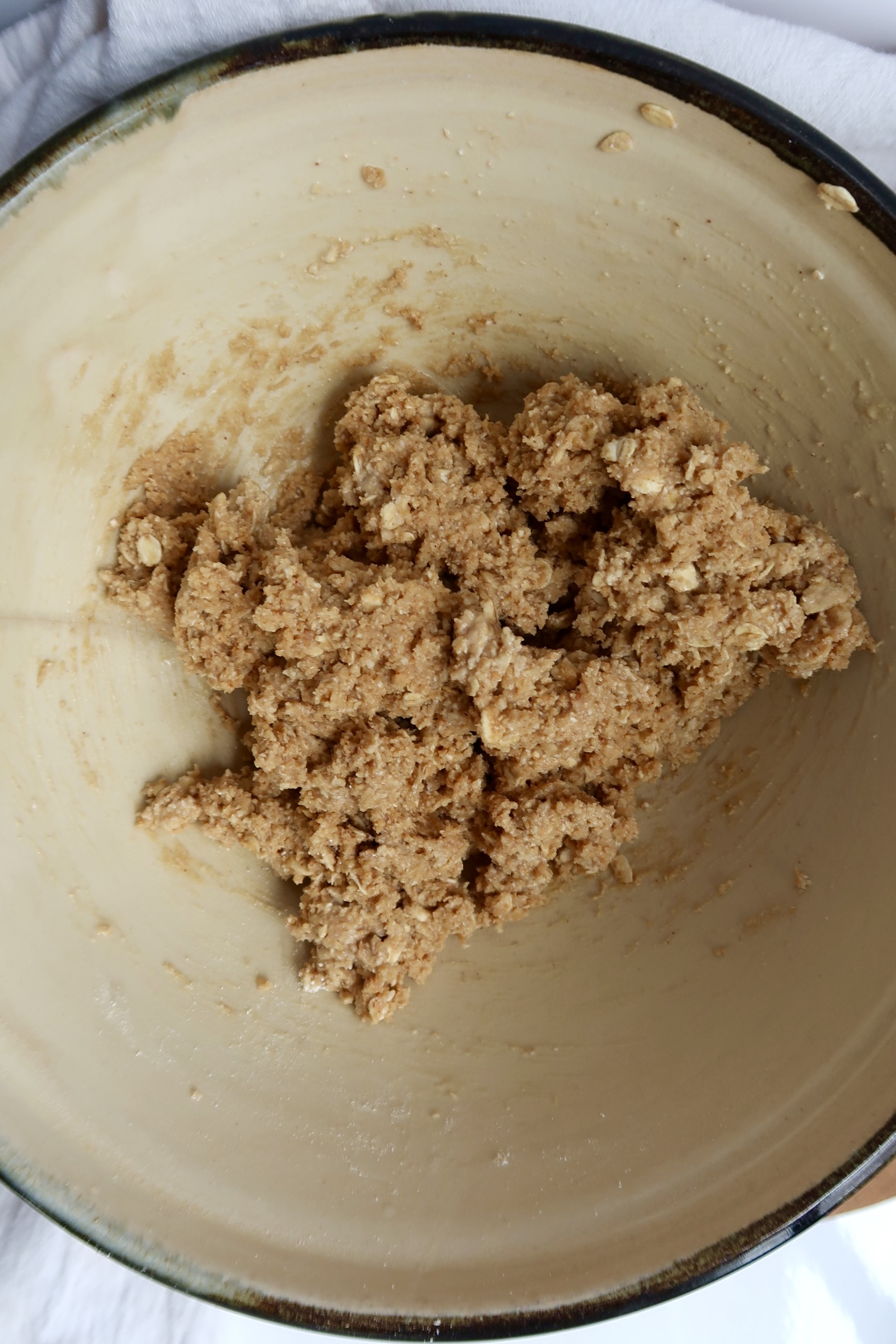 A mixing bowl containing a rough, beige dough mixture, likely for cookies or baked goods, with visible oats and a slightly sticky texture.
