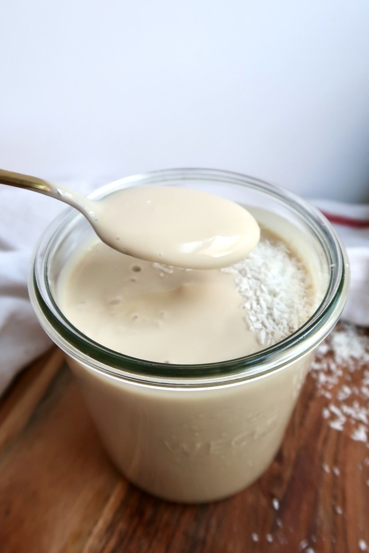 Glass jar with coconut pudding in it with coconut flakes on top and spoon scooping some.