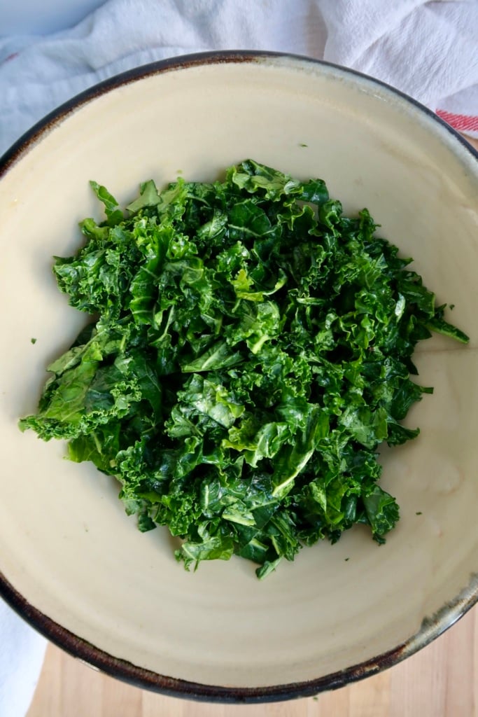A beige bowl filled with freshly chopped green kale, placed on a light-colored surface.