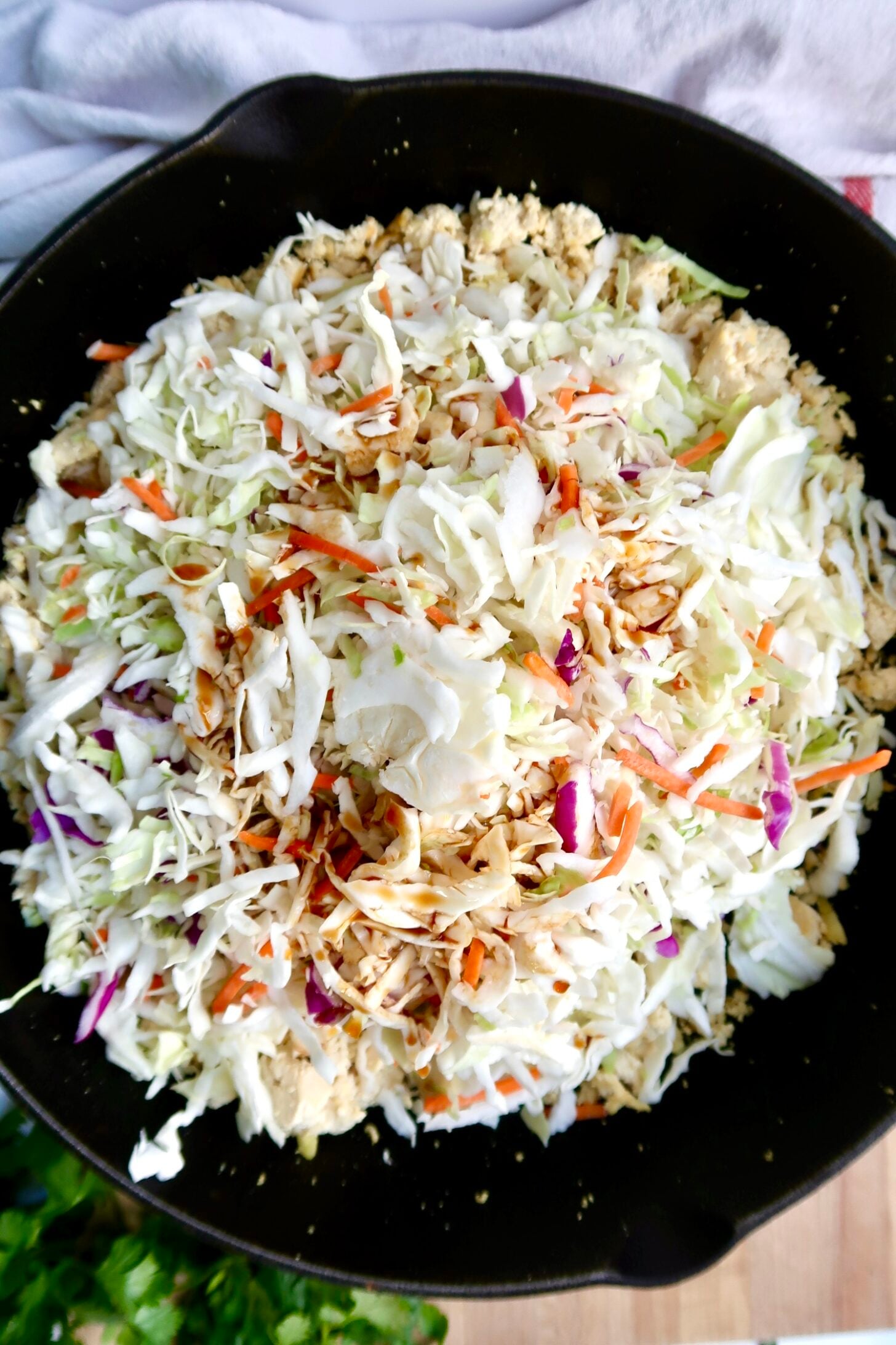 A close-up of a skillet filled with a mix of shredded cabbage, carrots, and purple cabbage, garnished with seasonings, ready to be cooked.
