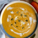 Bowl of carrot soup with coconut milk drizzled on top and pumpkin seeds on top.