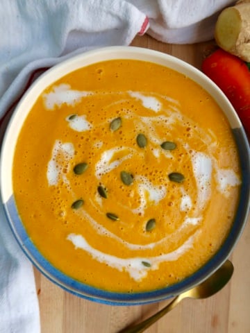 Bowl of carrot soup with coconut milk drizzled on top and pumpkin seeds on top.