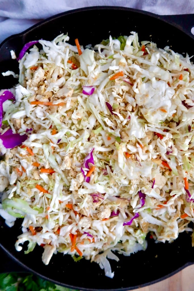 A close-up of a skillet filled with a colorful stir-fry of shredded cabbage, carrots, purple cabbage, and crumbled tofu. The vegetables are lightly cooked and mixed together.