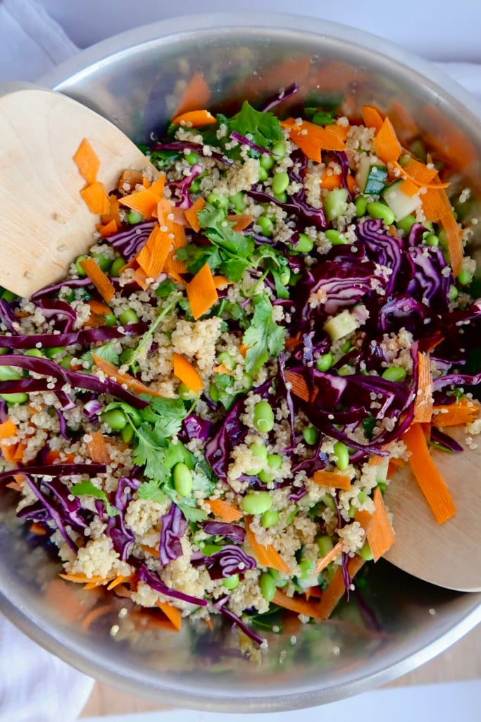 Salad tongs tossing quinoa, cabbage, shaved caorrots, edamame salad.