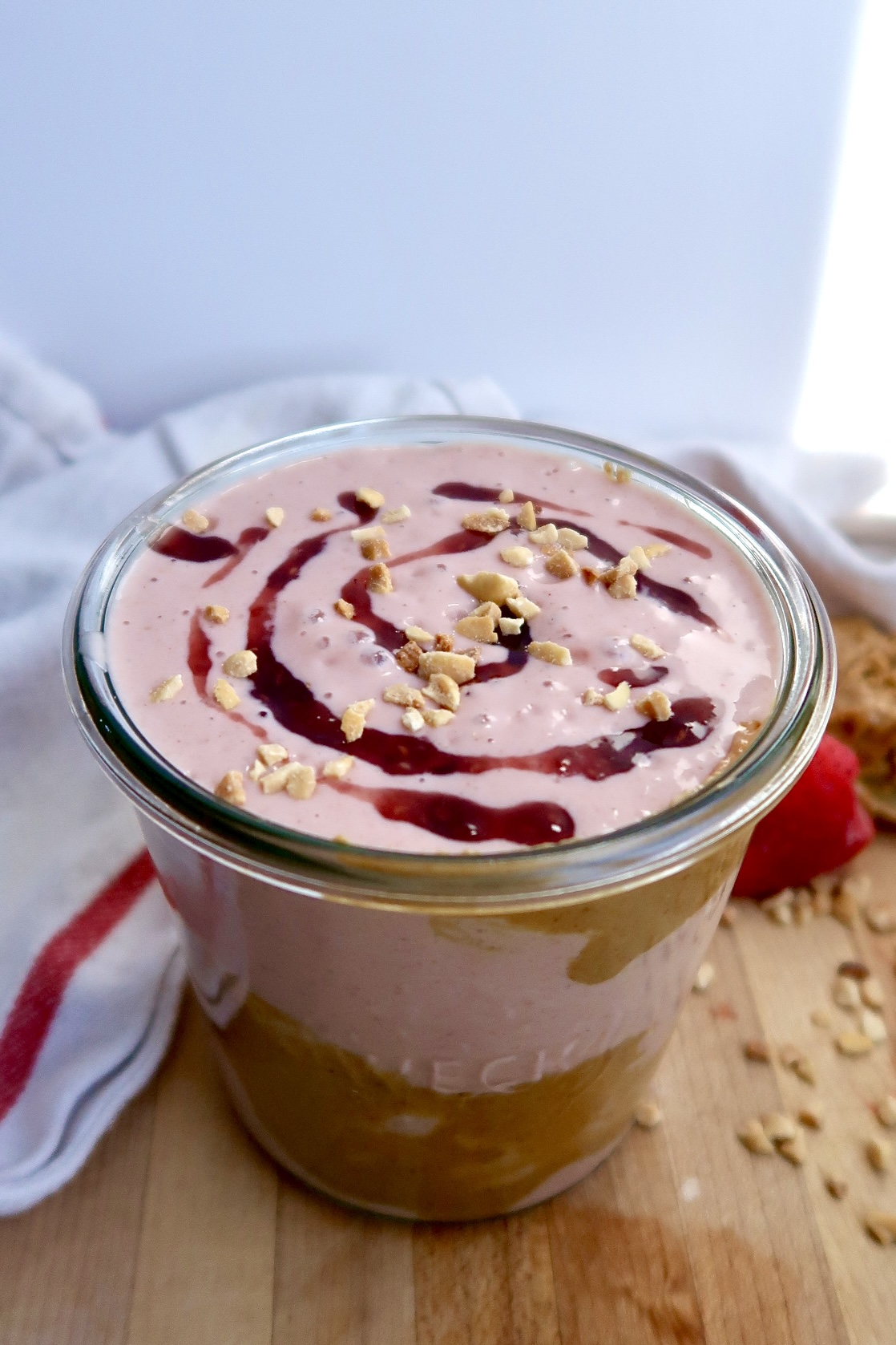 Strawberry smoothie on a cutting board with peanut butter around the jar on a cutting board.