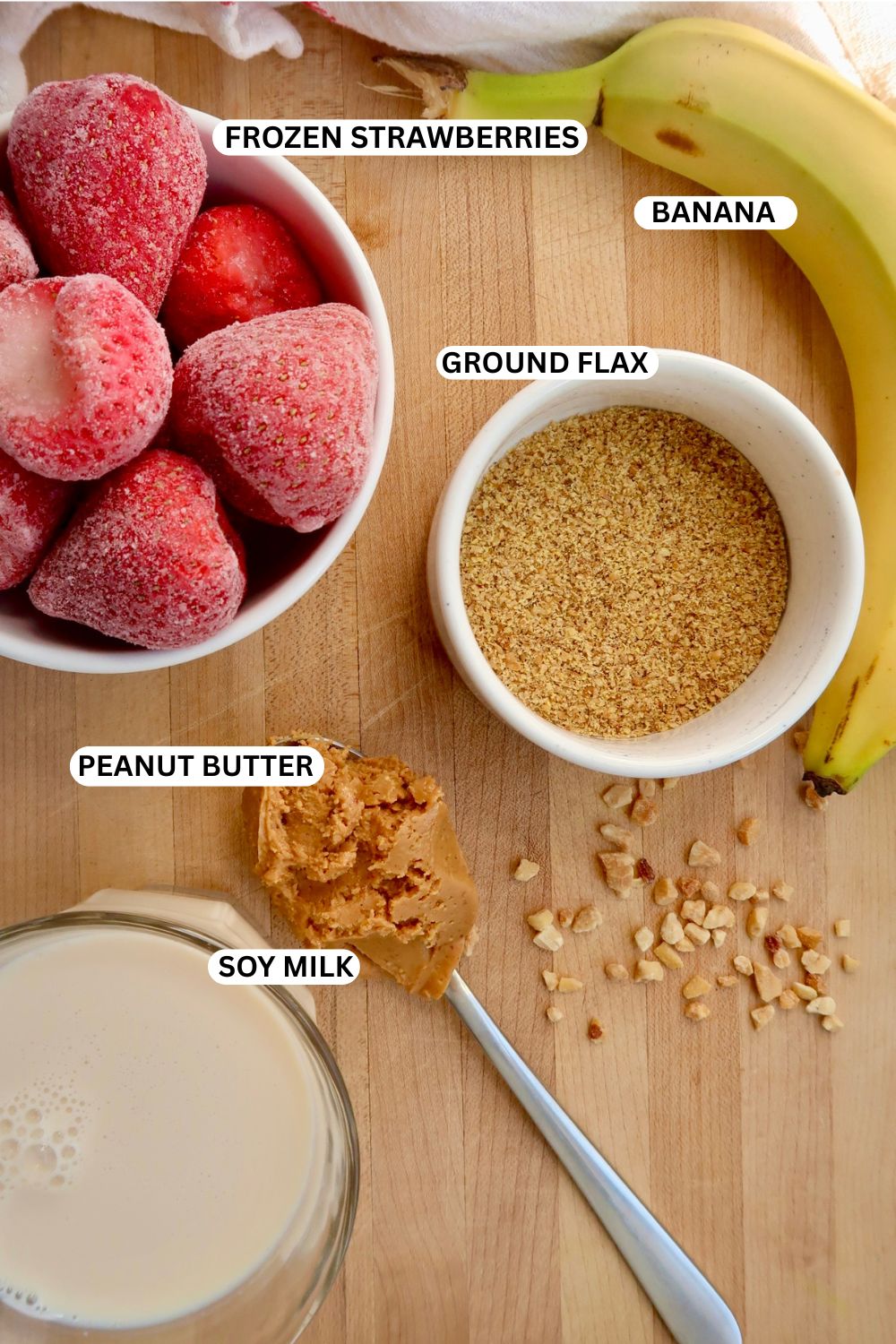 Flatlay of ingredients for the peanut butter and jelly smoothie like banana, strawberries, ground flax seeds, peanut butter and soy milk.