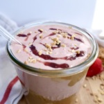 Strawberry smoothie on a cutting board with peanut butter around the jar on a cutting board with strawberries off to the side with a straw.