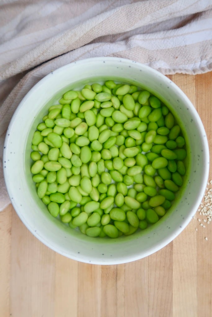 White bowl with shelled edamame with water on top.