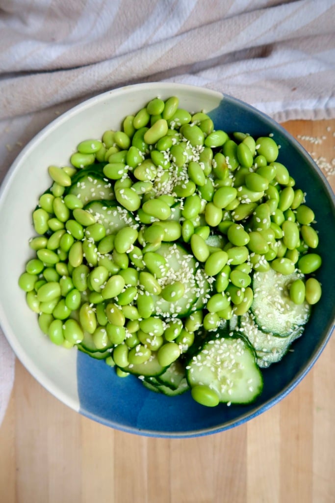 Blue and white bowl with edamame and cucumber inside with sesame seeds on top.