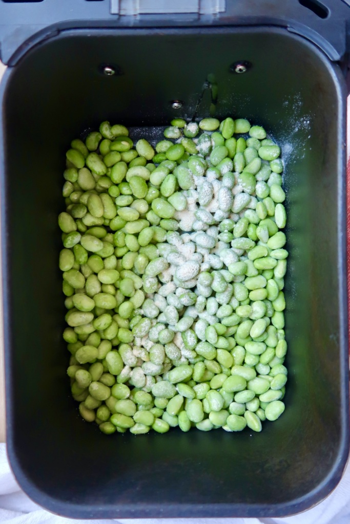 Air fryer basket with edamame pods and garlic powder sprinkled on top.