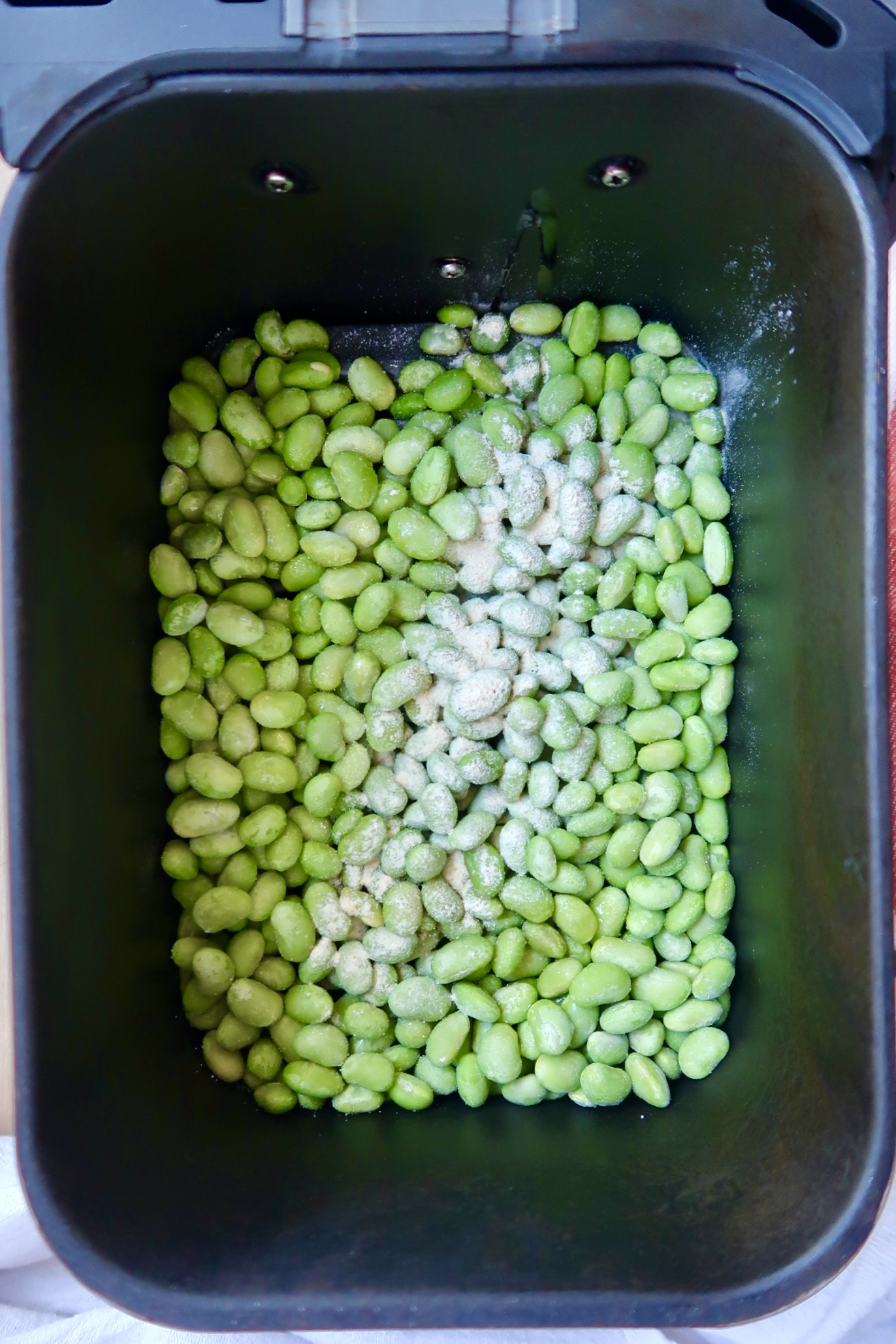 Air fryer basket with edamame pods and garlic powder sprinkled on top.
