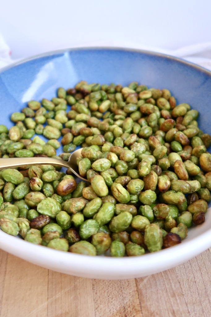Roasted edamame in a blue and white bowl with a spoon inside.