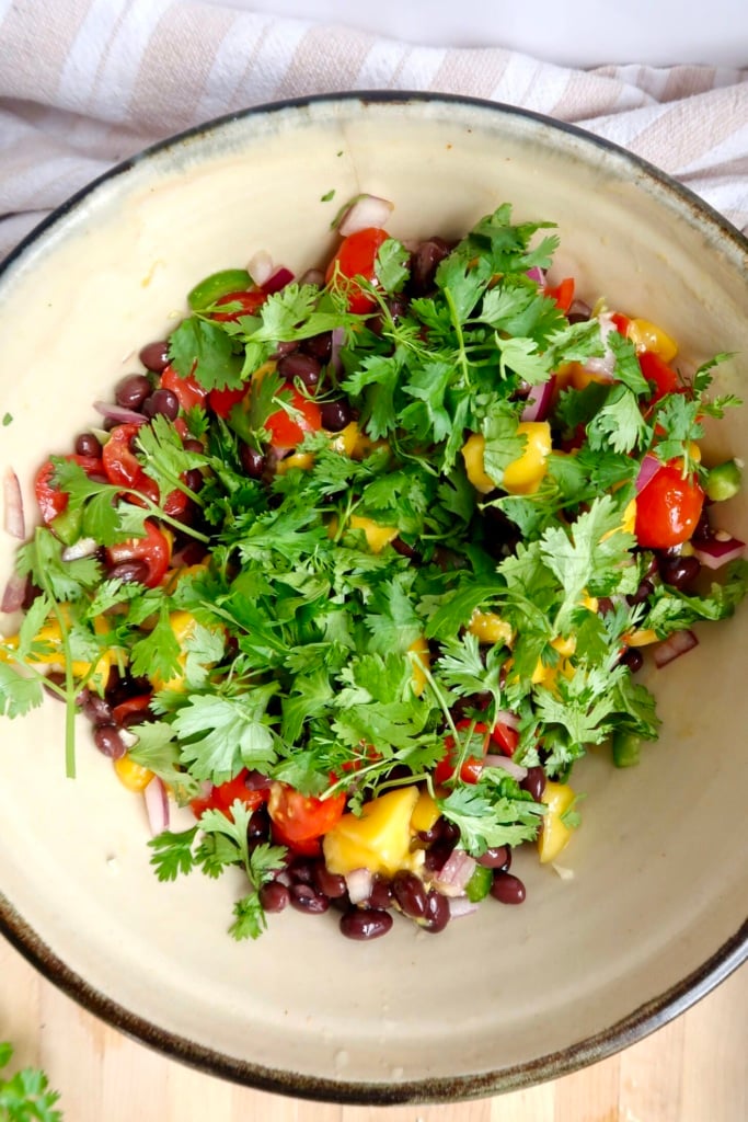 Cherry tomatoes, mango, black beans and cilantro in a bowl.