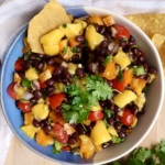 Mango black bean salsa in a bowl with cherry tomatoes, bell pepper and black beans with chips on the side.