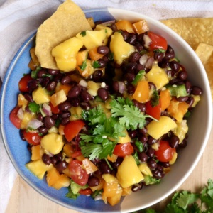 Mango black bean salsa in a bowl with cherry tomatoes, bell pepper and black beans with chips on the side.