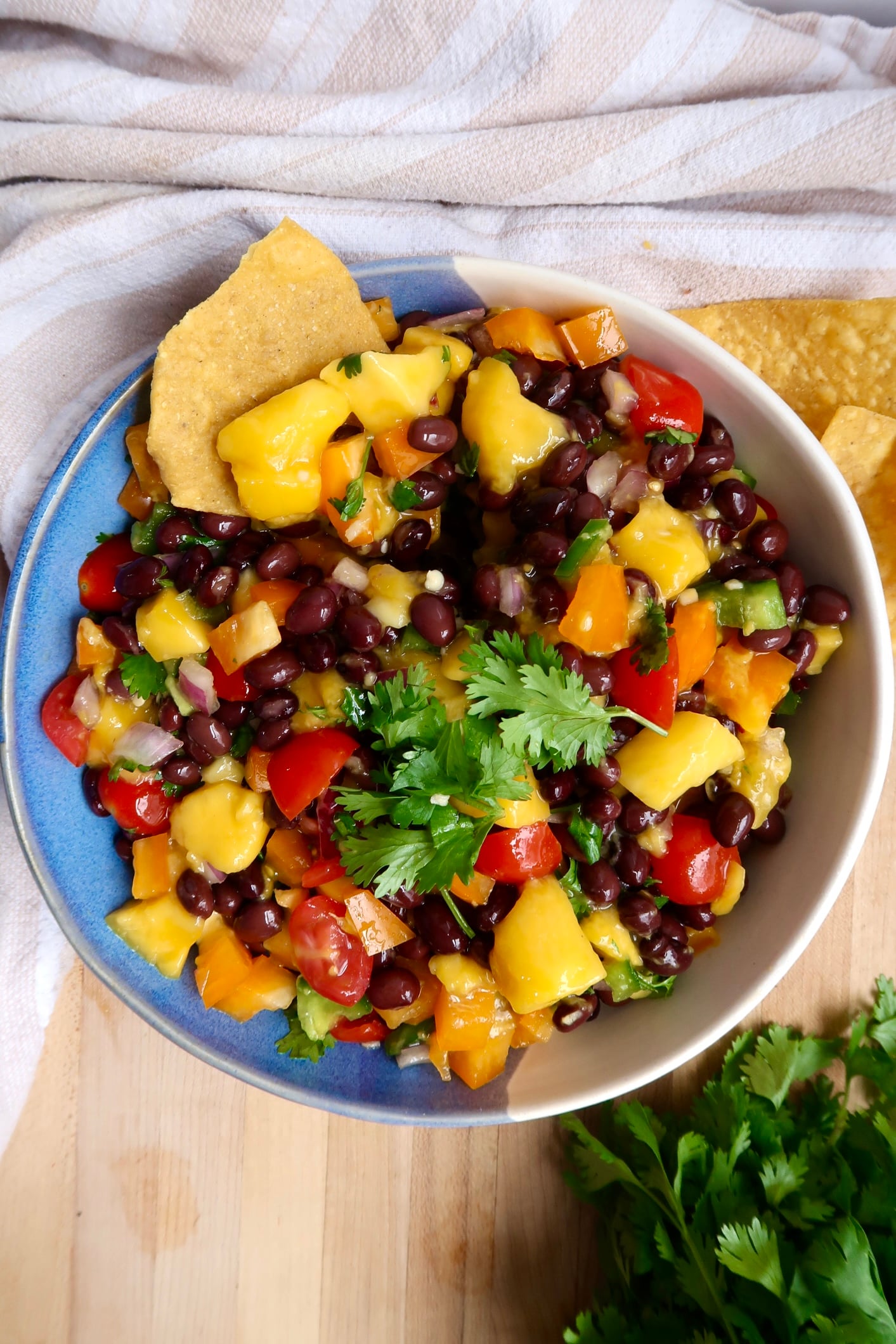 Mango black bean salsa in a bowl with cherry tomatoes, bell pepper and black beans with chips on the side.