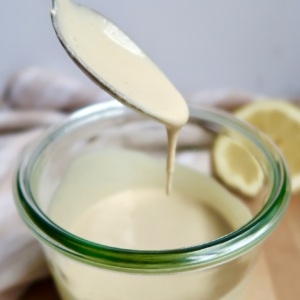 Glas jar with creamy sauce inside with a spoon scooping some and letting drip, with a lemon off to the side.