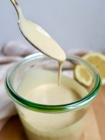 Glas jar with creamy sauce inside with a spoon scooping some and letting drip, with a lemon off to the side.