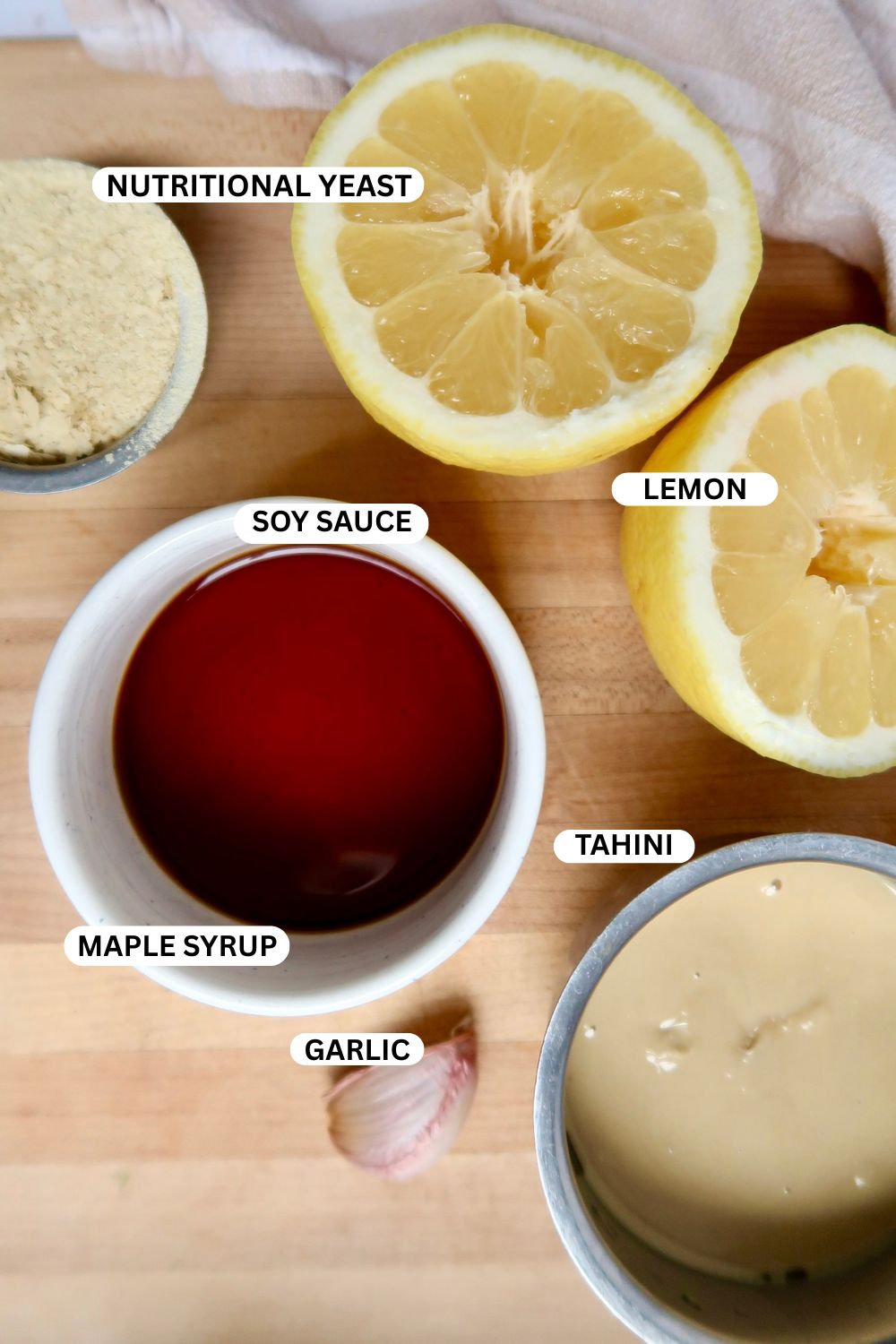 Cutting board with lemon, soy sauce, maple syrup, nutritional yeast, tahini and garlic on it.