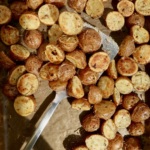 Roasted baby red potatoes on a sheet pan with spices on them and a spatula picking some up.