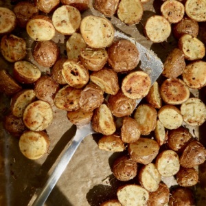Roasted baby red potatoes on a sheet pan with spices on them and a spatula picking some up.