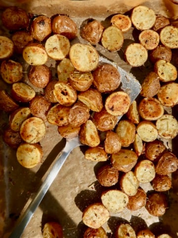 Roasted baby red potatoes on a sheet pan with spices on them and a spatula picking some up.