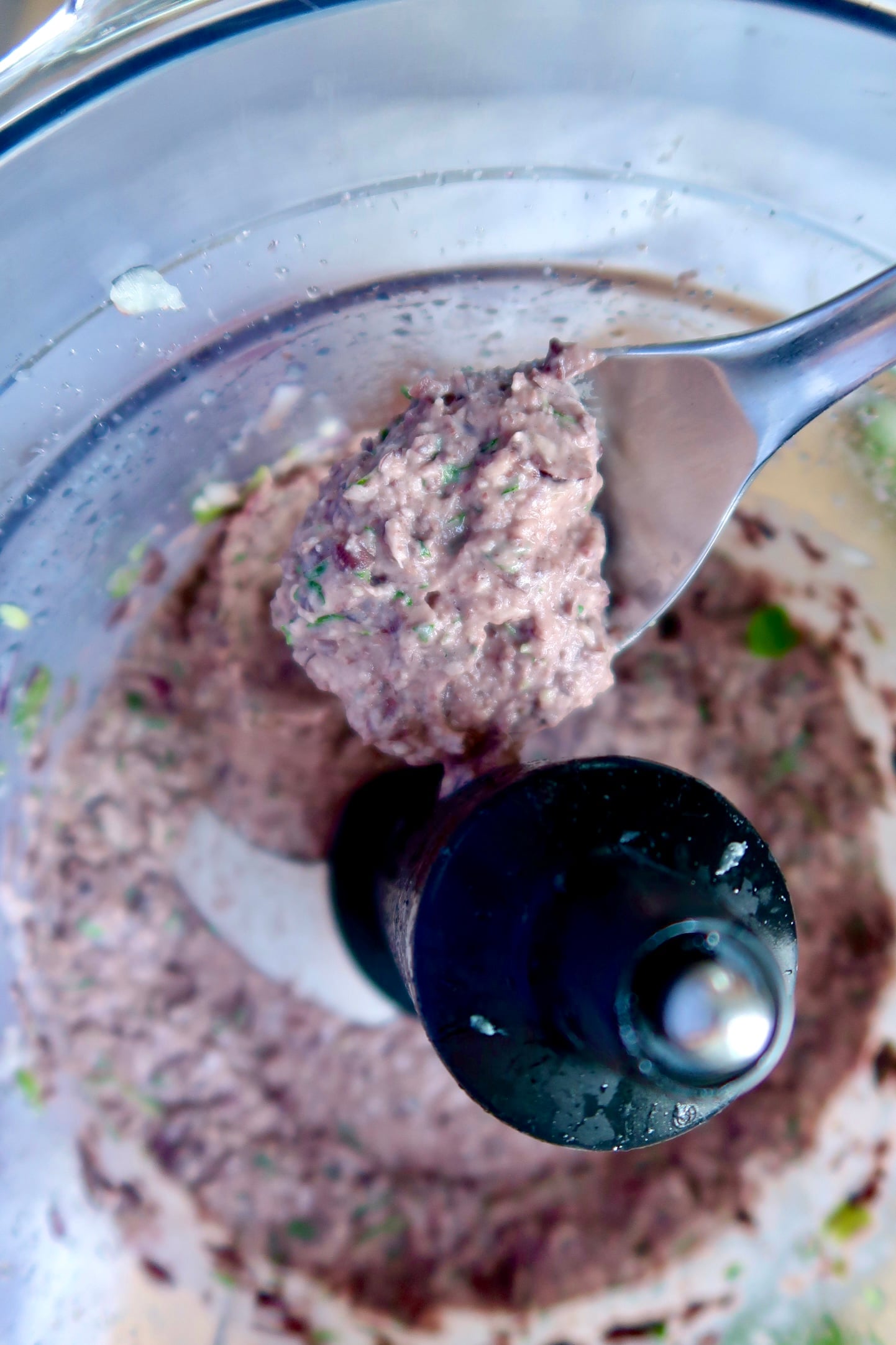 Blended black bean dip in a food processor with a spoon scooping some.