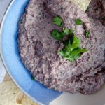 Blended black bean dip in a bowl with cilantro on top and chip being dipped inside.