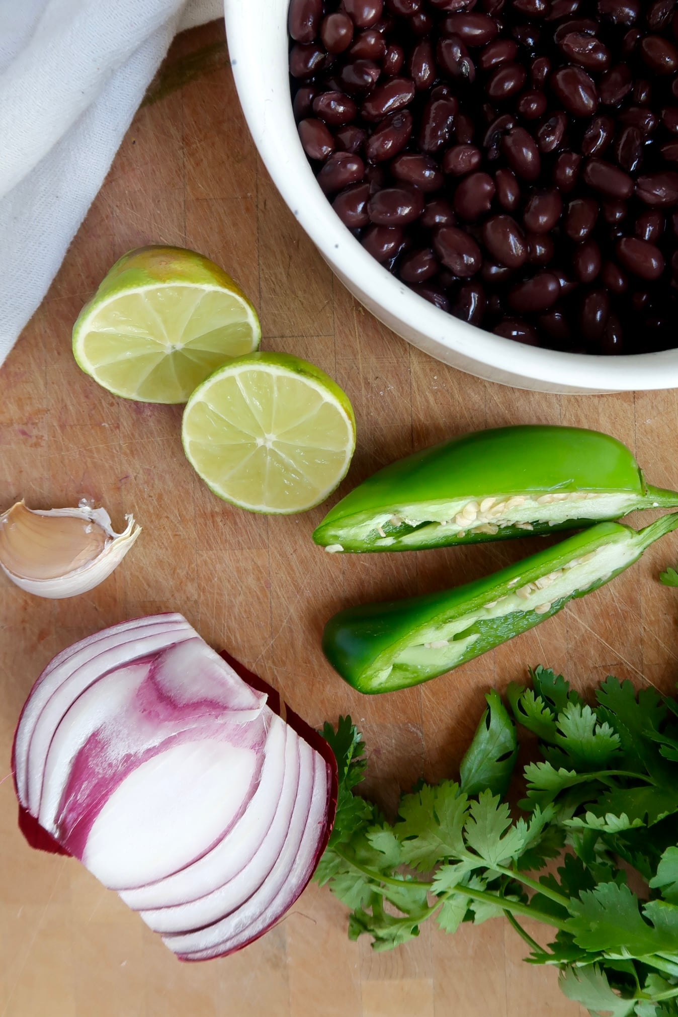 Cutting board with black beans in a bowl, lime, jalapeno, red onion, garlic and cilantro.