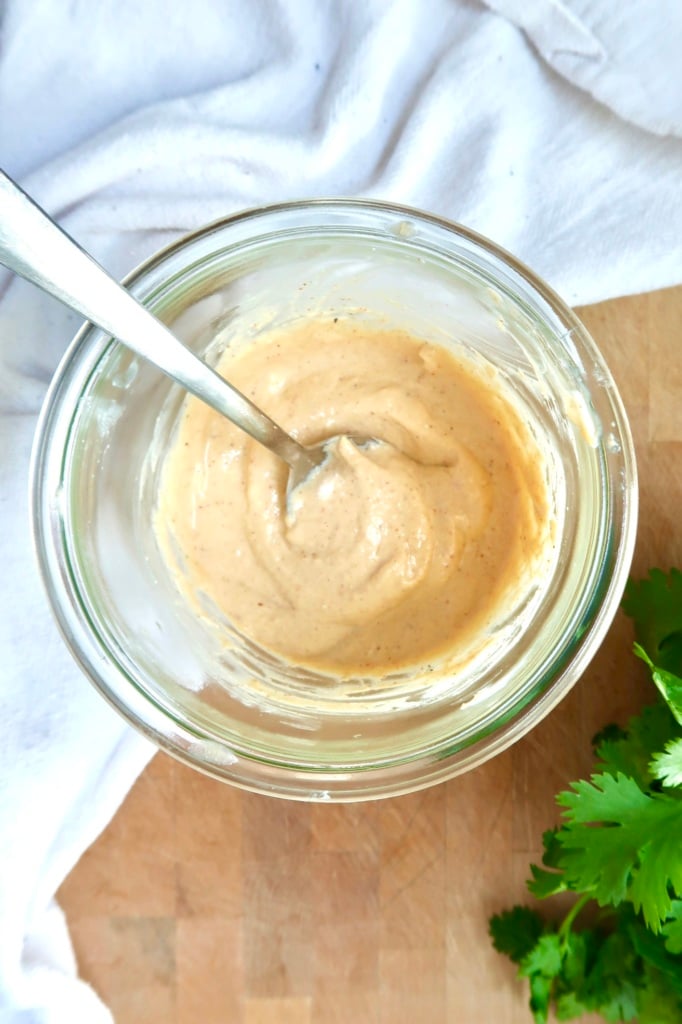 Jar with a creamy chipotle sauce inside, a spoon, and cilantro off to the side.