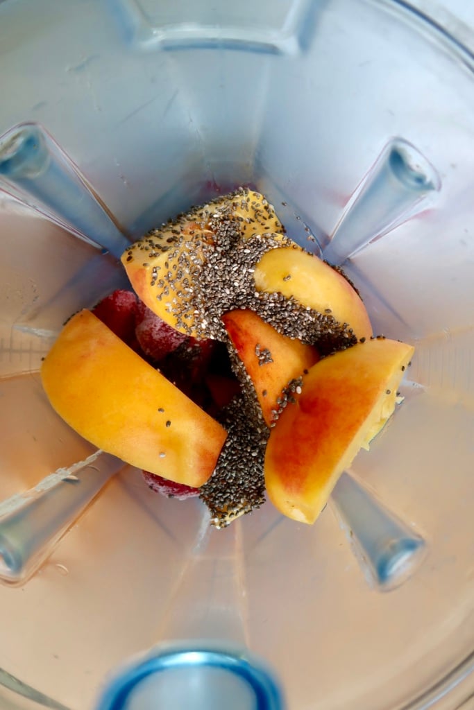 Blender container with sliced peaches, frozen strawberries and chia seeds.