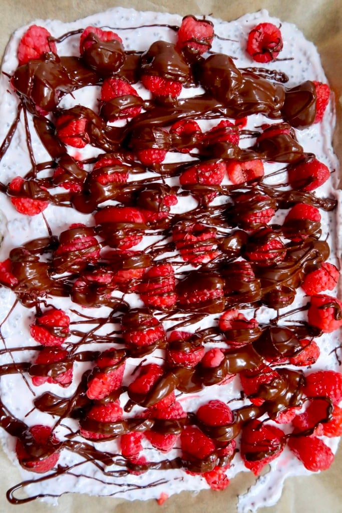 Top down view of yogurt on parchment paper with raspberries on top and chocolate drizzled on top.